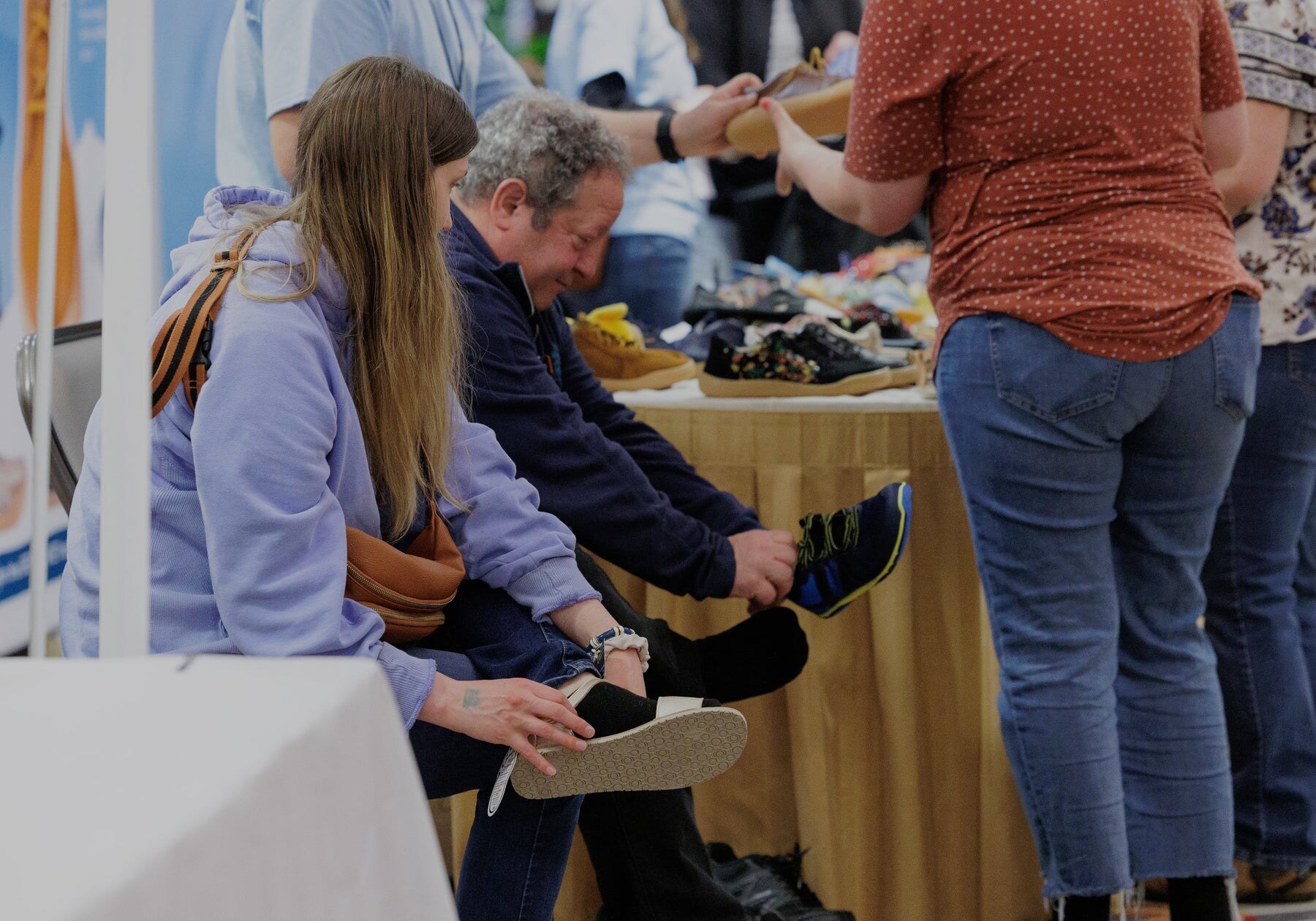 Visitors trying on barefoot shoes beside an exhibitor table, photo by Barefoot Shoe Expo