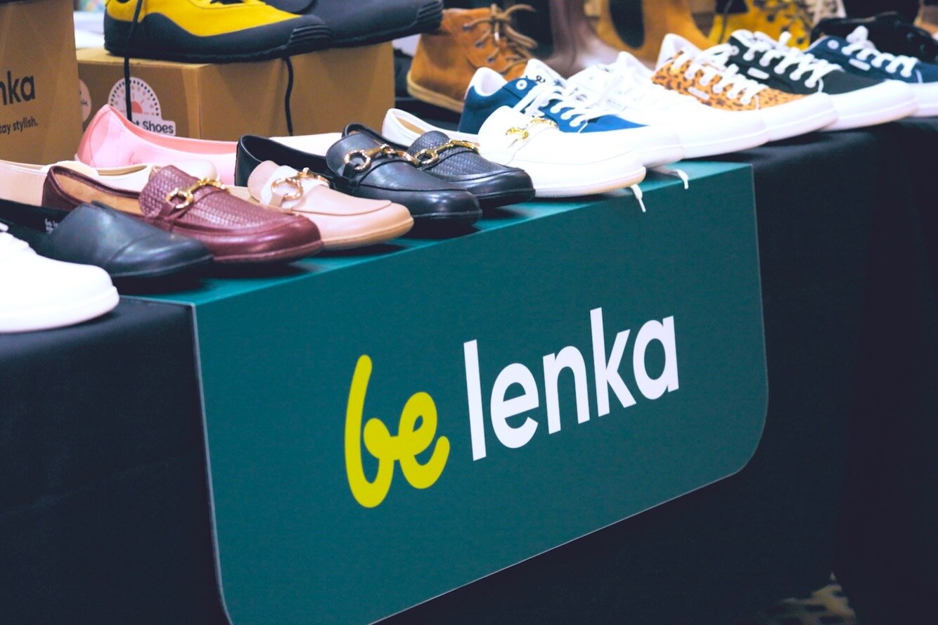 Barefoot shoes arranged above the Be Lenka stand banner, photo by The Foot Collective