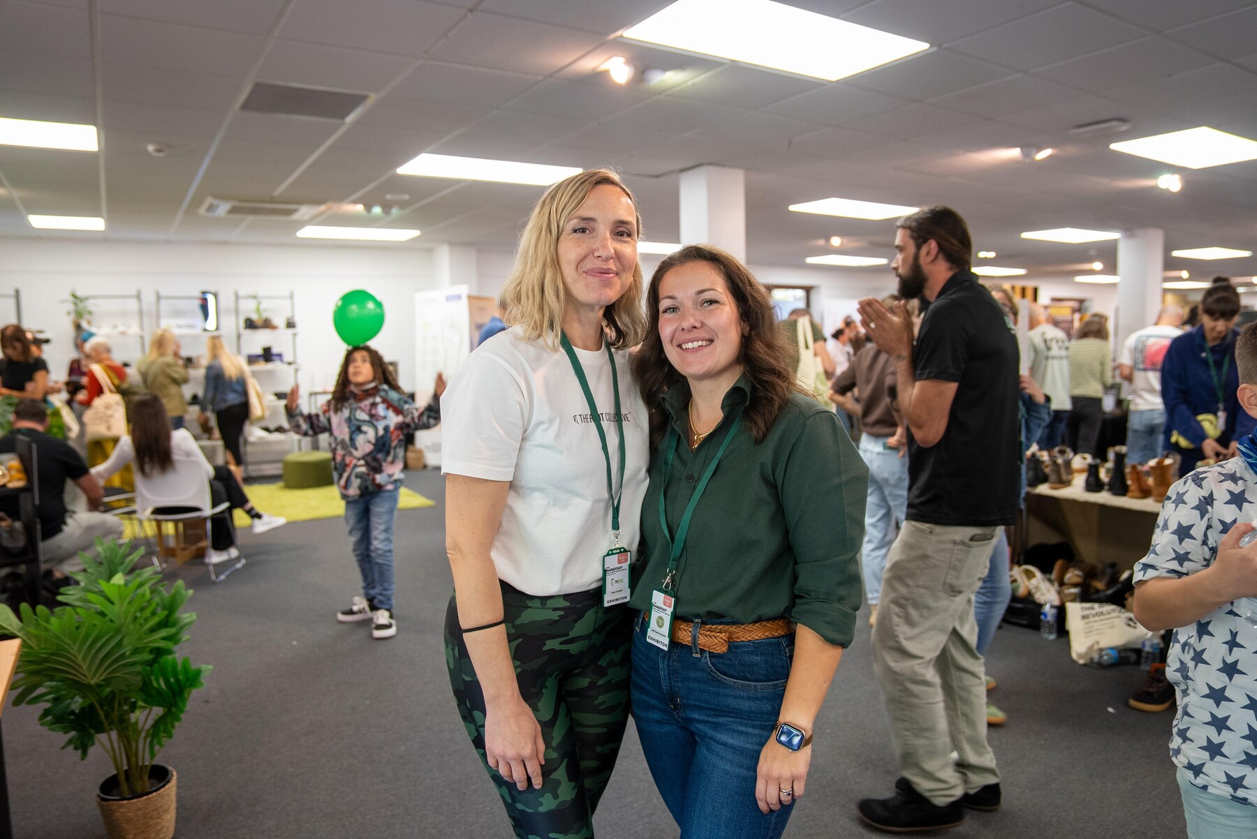 Two exhibitors smiling together on the busy show floor, photo by Barefoot Brit Expo