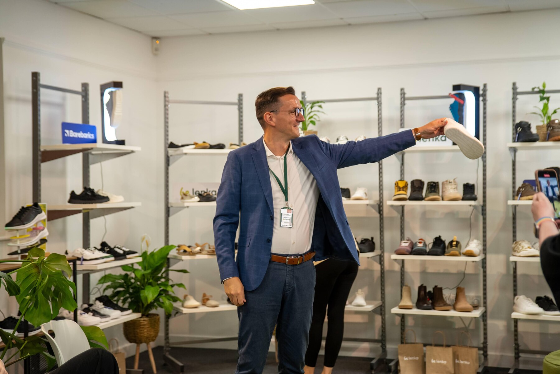 An exhibitor presenting a shoe beside shelves of footwear, photo by Barefoot Brit Expo