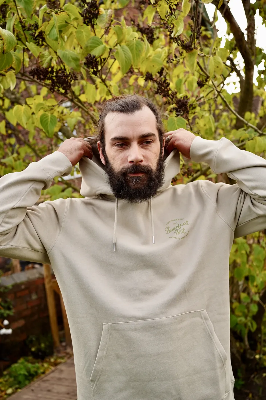 Dan pulling up the hood of a stone coloured Barefoot Brit hoodie in the garden