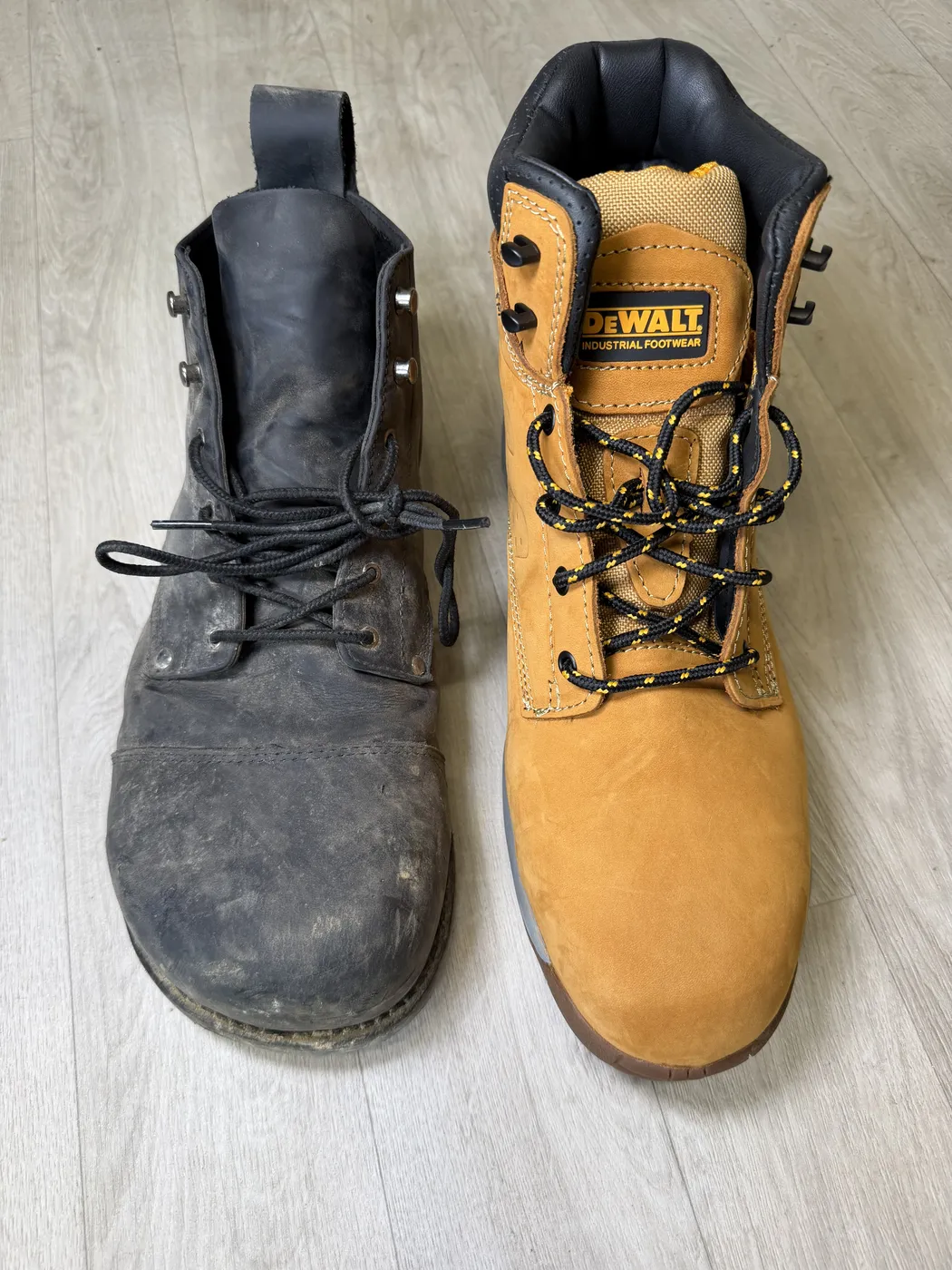 A worn black foot-shaped work boot next to a brand new tan conventional safety boot with a pointed toe